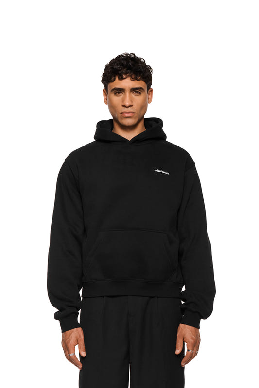 A man wearing a black hoodie with a hood and a kangaroo pocket, featuring a small white logo on the chest, paired with black sweatpants, against a white background.