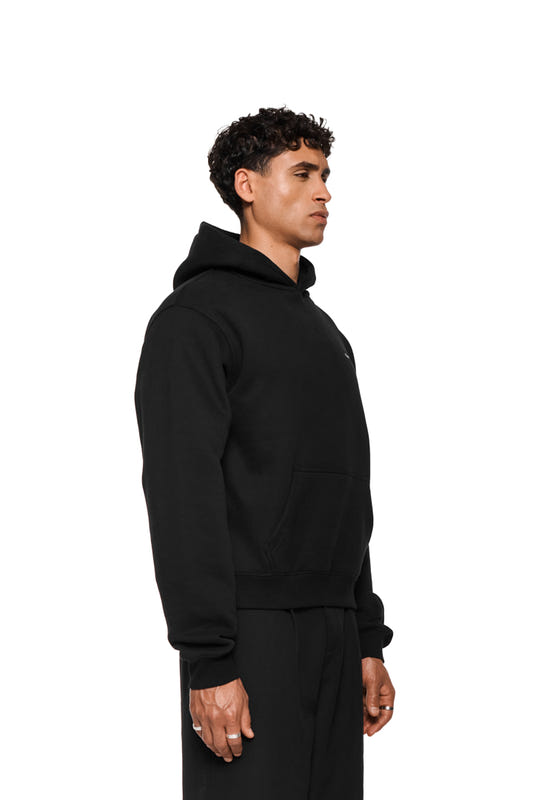 A side profile shot of a man wearing a black hoodie with a hood and a kangaroo pocket, and black sweatpants.
