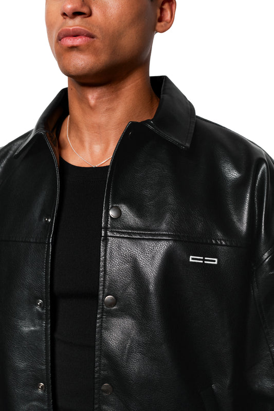 Mann trägt CC Leather Jacket Icon Black mit gesticktem OLAKALA-Logo, veganem Lederimitat, Druckknöpfen und feiner Silberkette, passend zur oversized, unisex Passform.
