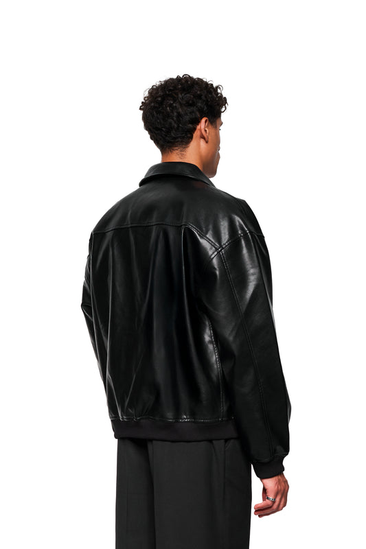 Mann mit OLAKALA CC Leather Jacket Icon Black, oversized Passform, veganem Leder, gesticktem Icon links, Verschlussdetail. Trägt lockere schwarze Hose, silbernen Ring am rechten Mittelfinger.