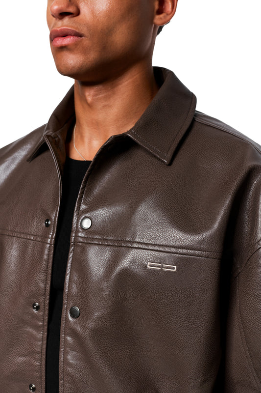 Person trägt die CC Leather Jacket Icon Brown aus veganem Lederimitat mit Druckknopfverschluss, gesticktem OLAKALA-Icon und übergroßer Passform, darunter schwarzes Oberteil.