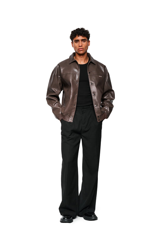 Ein Model trägt die CC Leather Jacket Icon Brown aus veganem Lederimitat mit Druckknöpfen und gesticktem OLAKALA-Icon, kombiniert mit schwarzem Shirt und Hose.