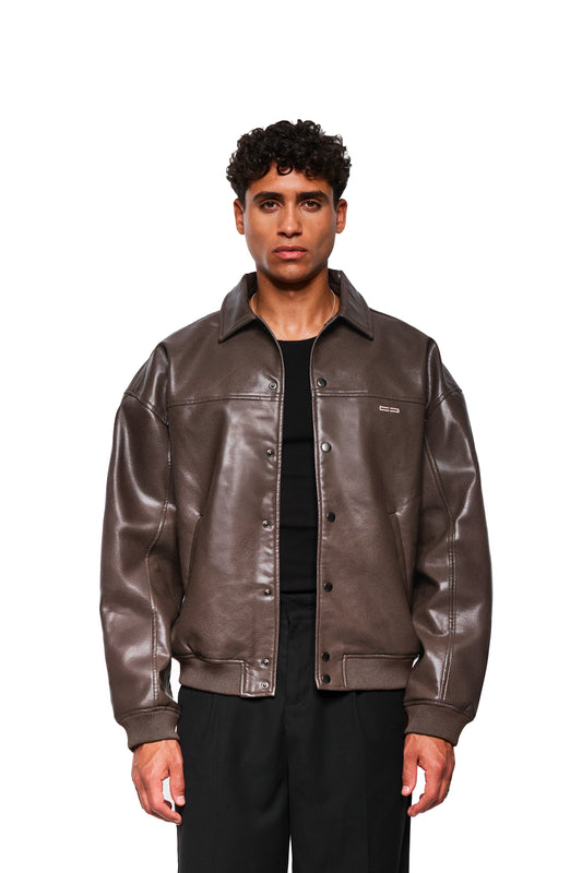 Männliches Model in brauner CC Leather Jacket Icon mit klassischem Kragen, Snap-Verschlüssen, Leistentaschen, OLAKALA-Stickerei, oversized Passform.