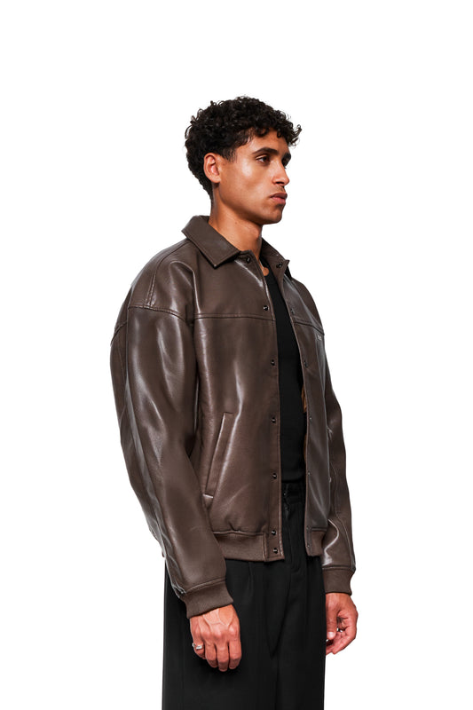 Junger Mann trägt die CC Leather Jacket Icon Brown aus veganem Lederimitat mit gesticktem OLAKALA-Icon und Leistentaschen, präsentiert in Oversized-Unisex-Design.