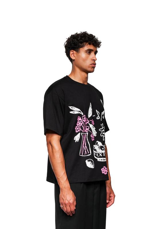 Junger Mann im Profil trägt das Crayon T-Shirt Oversized Black mit weißen und pinken Skizzen. Lockerer Schnitt, unisex, entspannter Stil.