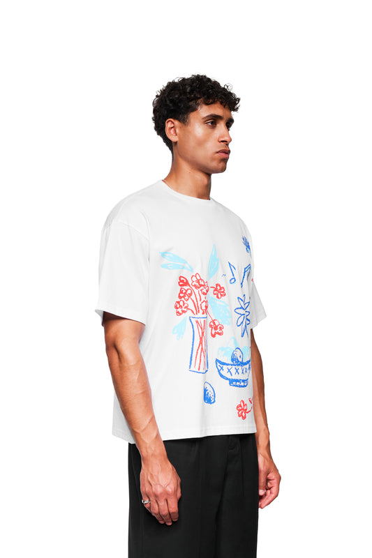 Junger Mann im Profil trägt Crayon T-Shirt Oversized White mit handgezeichneten Grafiken, lockerer Passform und Ripp-Kragen, kombiniert mit schwarzen Hosen.