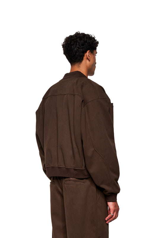 Exquisite Bomber Jacket Brown: Back view of a model with a loose, brown bomber jacket set, ribbed stand-up collar, breast pocket, back pleats and embroidered OLAKALA icon.