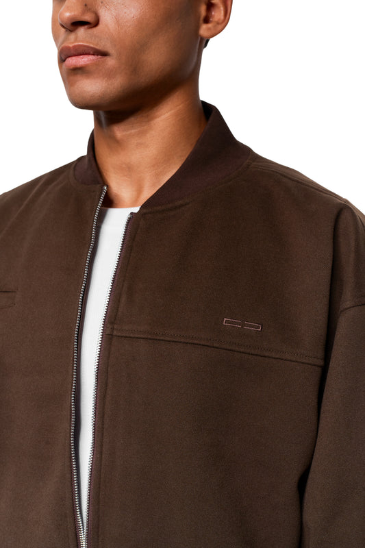 Person in Exquisite Bomber Jacket Brown with ribbed collar, chest embroidery and zipper, worn over a white T-shirt. Unisex and loose fit.