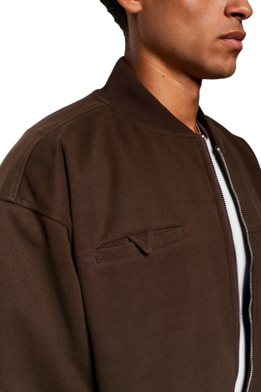 Person wears the Exquisite Bomber Jacket Brown with zipper, ribbed stand-up collar and chest pocket. Dart details and embroidered OLAKALA icon visible.