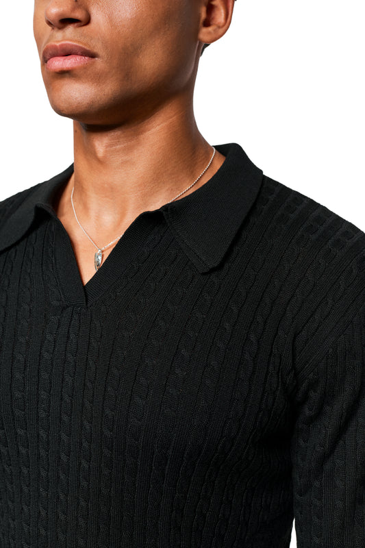 Person wears Exquisite Cable Knit Polo Black, a black, close-fitting, cable-knit sweater with a V-neck, polo collar and fine knit details, with a silver necklace.