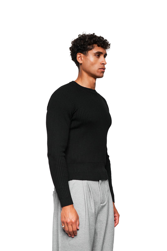 Junger Mann im Profil trägt den Exquisite Knit Longsleeve Black mit eng anliegender Passform und unterschiedlichen Strickmustern an Bund und Ärmeln.