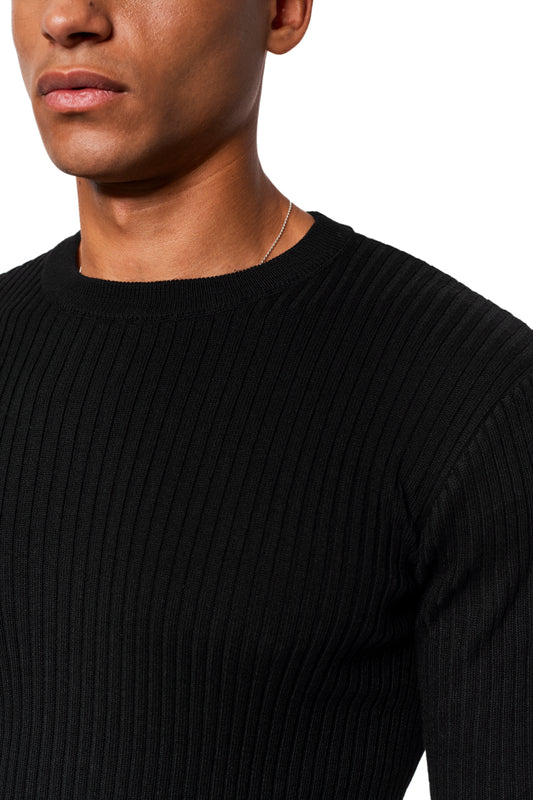 Man wears Exquisite Knit Longsleeve Black, black ribbed sweater with knitted cuffs; silver chain visible on the collar, emphasizes unisex design and tight fit.