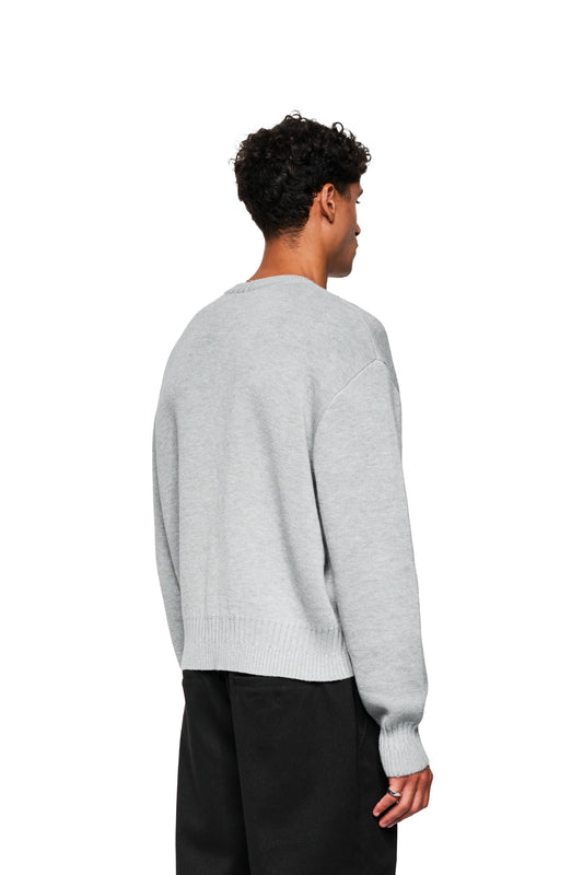 Back view of a man in the Exquisite Knit Sweater Gray with embroidered OLAKALA icon, loose fit, knitted cuffs and various knitting patterns.