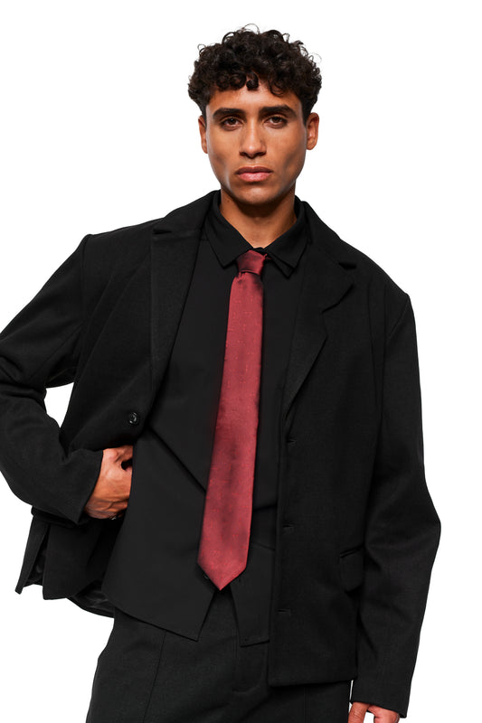 Junger Mann in schwarzem Anzug mit Monogram Tie Bordeaux, Krawatte mit Monogramm-Muster, präsentiert formell, Hand in Jackentasche, bei OLAKALA erhältlich.