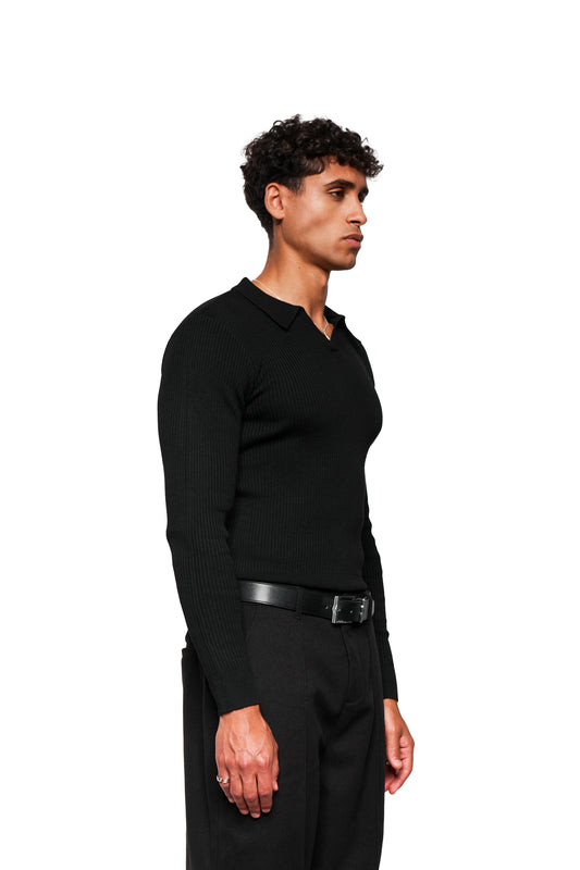 Junger Mann im Profil trägt Exquisite Rib Knit Polo Black; figurbetont mit Doppelkragen-Detail links, kombiniert mit schwarzer Hose und silbernem Schmuck.