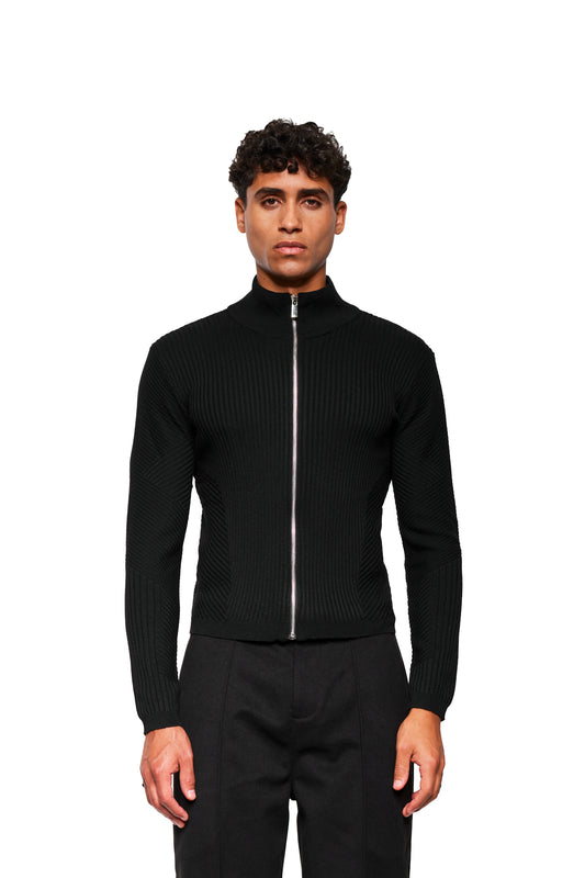 Männliches Model trägt Exquisite Knit Jacket Black mit körperbetonendem Strickmuster, Stehkragen, silbernem Reißverschluss und angestrickten Bündchen, kombiniert mit geraden schwarzen Hosen.