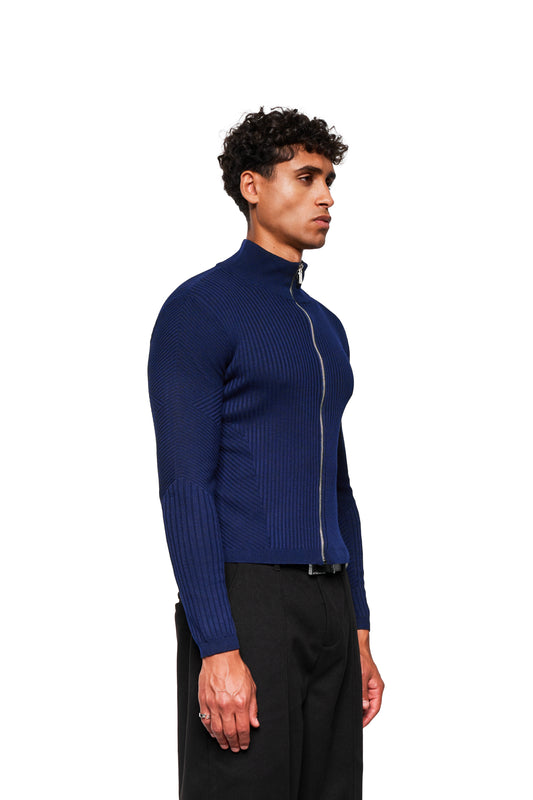 Junger Mann in Profilansicht trägt Exquisite Knit Jacket Navy Blue mit anatomischem Strickmuster, Stehkragen und silbernem Reißverschluss, kombiniert mit lockeren schwarzen Hosen.