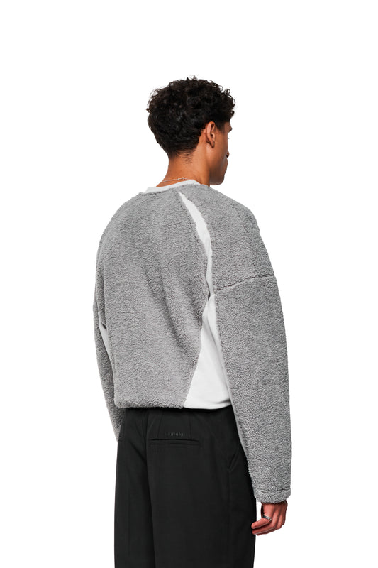 Rückansicht eines Mannes im Fleece V-Neck Sweater Gray mit elastischem Saum und gesticktem OLAKALA Stuttgart Logo, kombiniert mit schwarzen Hosen.