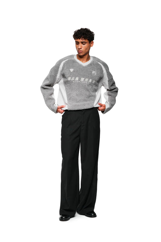 Young man wears fleece V-neck sweater gray with embroidered OLAKALA Stuttgart logo, sporty icons and adjustable hem, combined with black pants and leather shoes.