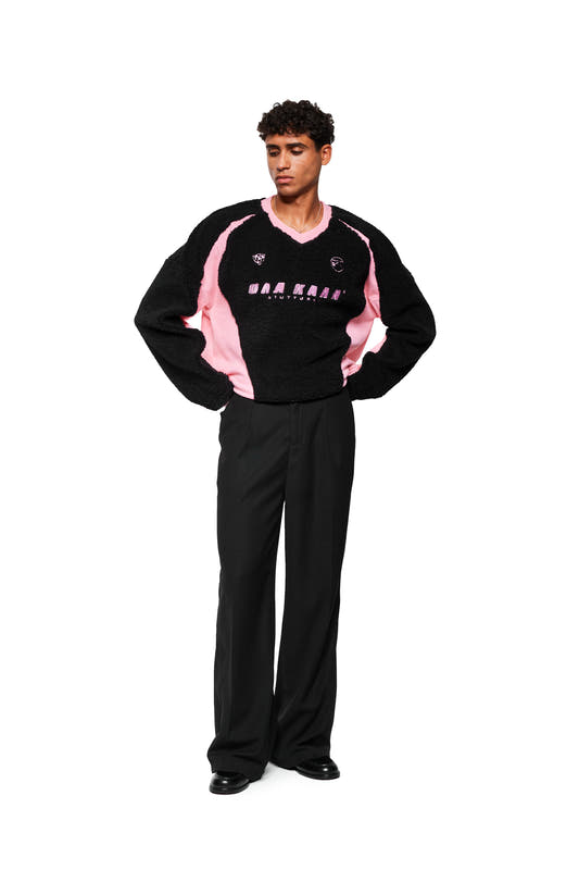 A young man wears the Fleece V-Neck Sweater Pink with embroidered icons and adjustable hem, presented by OLAKALA.
