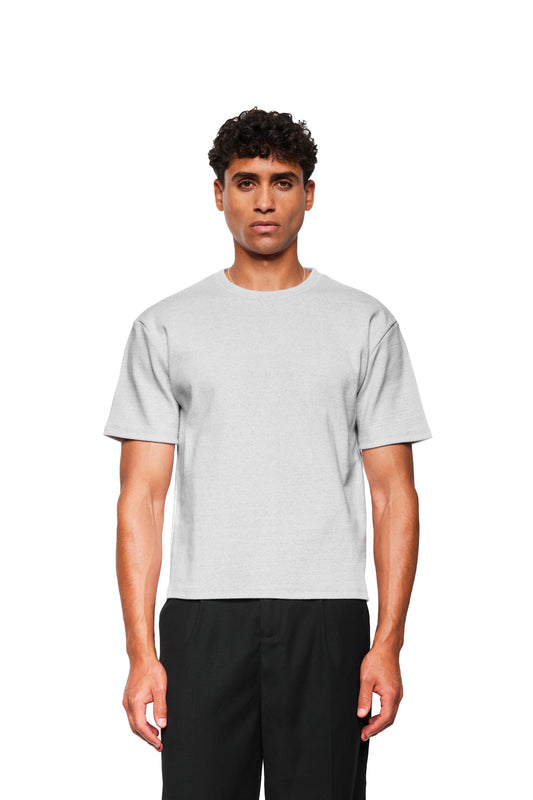 Männliches Modell trägt ein Exquisite Rib T-Shirt Gray Melange aus festem Rippstoff mit lockerer Passform, kombiniert mit schwarzen Hosen, vor weißem Hintergrund.