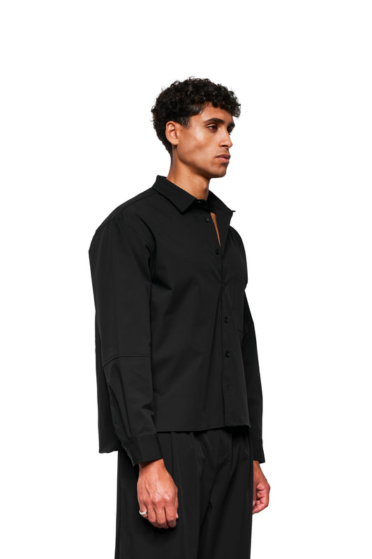 Junger Mann im Profil trägt Exquisite Tech Shirt Black mit doppeltem Kragen, Brusttasche mit Stickerei und lockerer Passform.
