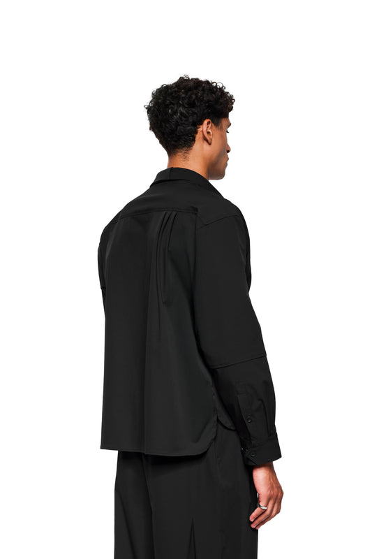 Exquisite Tech Shirt Black: Back view of the loose-fitting shirt with pleats on the back, double collar, breast pocket and rounded hem, worn by a male model.