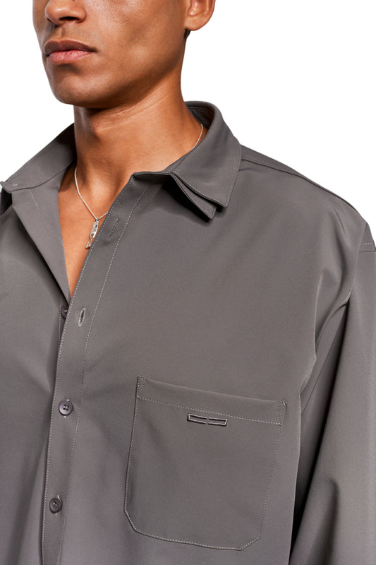 Man wears Exquisite Tech Shirt Gray with chest pocket and contrast stitching, combined with silver chain. Emphasis on robust, stretchy material and a loose fit.