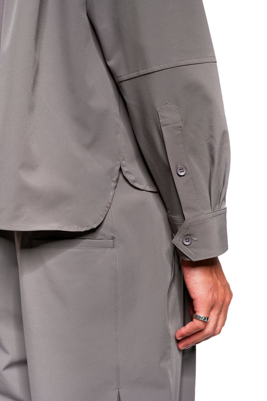 Person wears the Exquisite Tech Shirt Gray with rounded hem and side slit, shirt hem details and trouser pockets are visible. Silver ring on the hand.