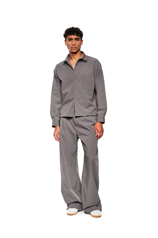 Model wearing Exquisite Tech Pants Gray with asymmetric pocket opening and pleats, combined with a matching shirt and white sneakers. Ideal for casual, stylish outfits.