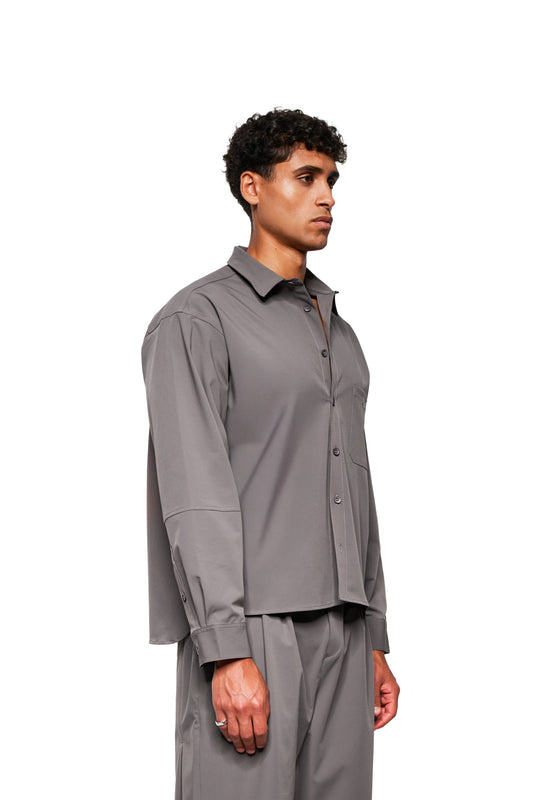 Männliches Modell in Profilansicht trägt das Exquisite Tech Shirt Gray mit doppeltem Kragen, Brusttasche und lockerer Passform, aus dehnbarem Material.