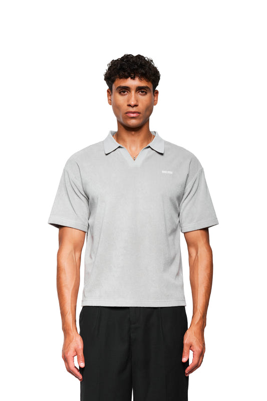 Male model wears Terry Polo Gray made of soft terry cloth material with logo embroidery on the chest, combined with black pants, against a white background.