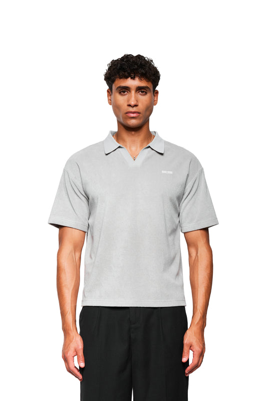 Männliches Modell trägt Terry Polo Gray aus weichem Frotteematerial mit Logo-Stickerei auf der Brust, kombiniert mit schwarzen Hosen, vor weißem Hintergrund.