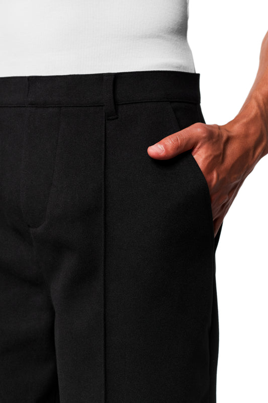 Close-up of Exquisite Dress Pants Black with loose fit and piping, worn with right hand in side pocket.