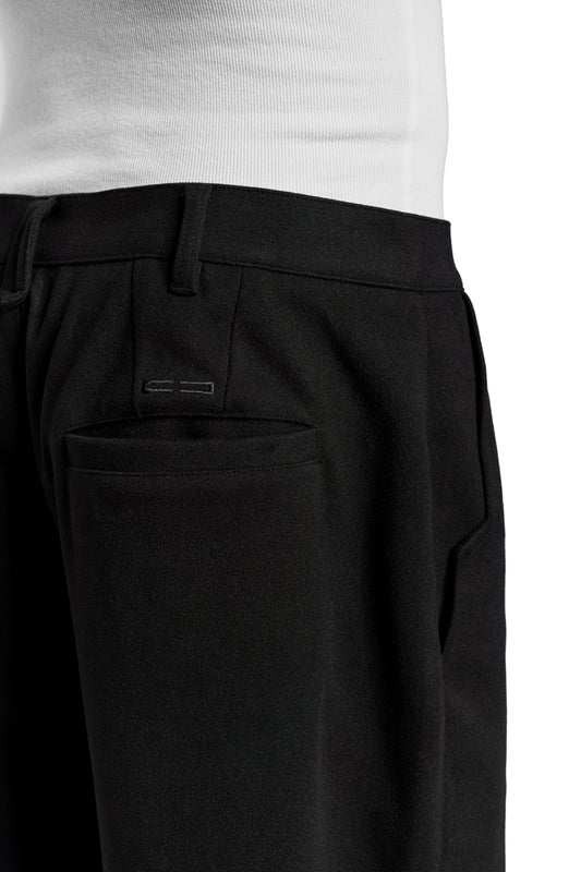 Close-up of a person wearing Exquisite Dress Pants Black, with visible piping, offset side seam and embroidered OLAKALA icon above the right back pocket.