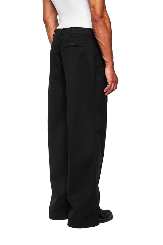 Back view of a person in Exquisite Dress Pants Black with wide leg, tucks, side zipper, embroidered OLAKALA icon and black slip-on shoe.