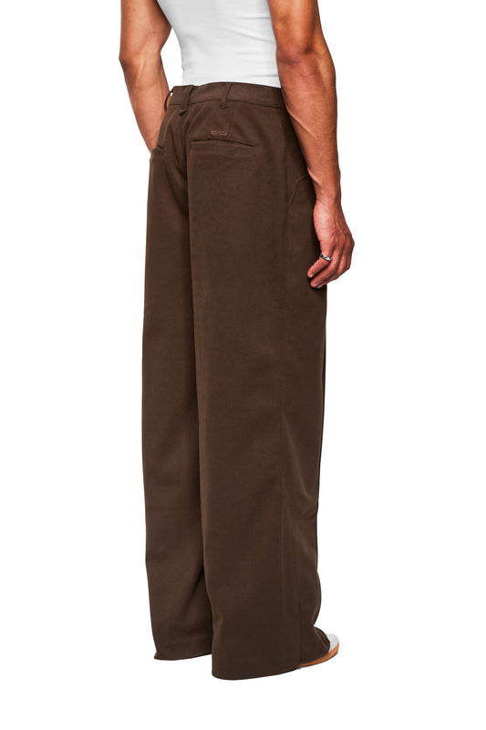 Person from behind in Exquisite Dress Pants Brown. Wide leg, pleats, side zipper. Silver ring on the hand; toe of shoe visible.