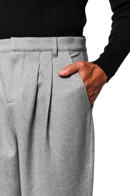 Person wearing Exquisite Dress Pants Gray with pleats and offset side seam, right hand in pocket. Embroidered OLAKALA icon visible.