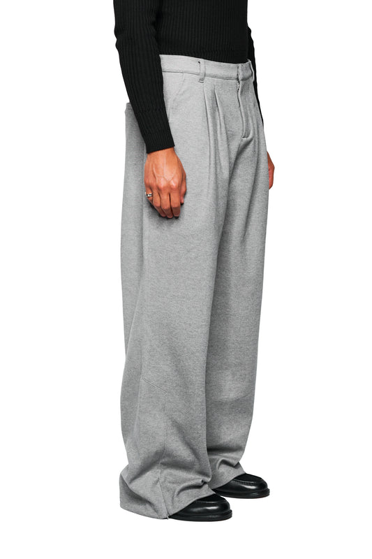 Exquisite Dress Pants Gray, locker geschnittene, hellgraue Hosen mit Bundfalten, weiten Beinen, die um schwarze Loafer fließen, und OLAKALA-Stickerei über der Gesäßtasche.