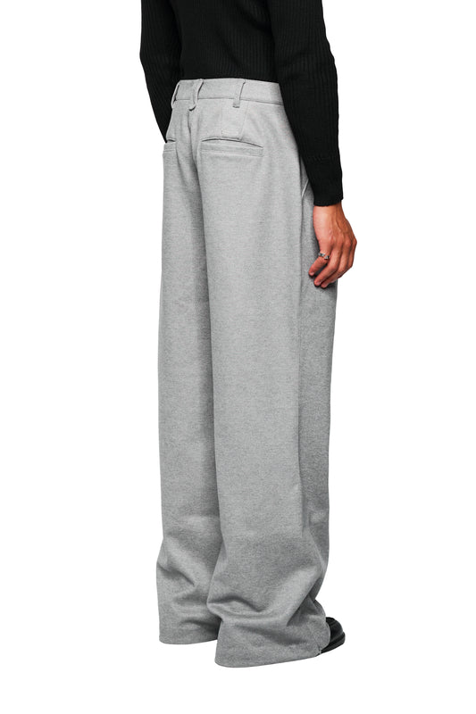 Person wears Exquisite Dress Pants Gray, loose-fitting, light gray pants with pleats. Visible are black shoes and a ring on the hand.