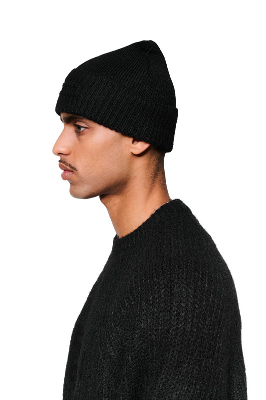 Profilansicht eines jungen Mannes mit Fuzzy Beanie Black, schlichtes Design, breiter Umschlag mit embossed Logo, vielseitiges Accessoire für kalte Tage.