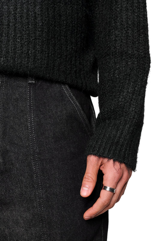 Unterer Rumpf mit Fuzzy Knit Sweater Black von OLAKALA, gerippte Struktur, silberner Ring am Finger, kontraststichige Hose sichtbar.