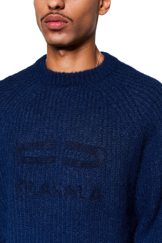 The person is wearing the Fuzzy Knit Sweater in Navy Blue, featuring a chunky ribbed pattern and subtle logo embroidery on the chest.