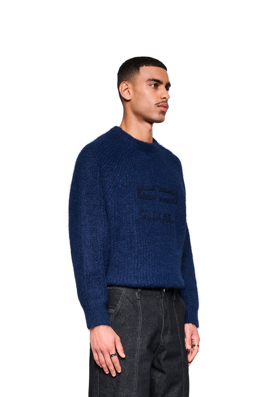 Männermodell im Fuzzy Knit Sweater Navy Blue mit cropped, boxy Silhouette und großer Logo-Stickerei, kombiniert mit dunklen Jeans.