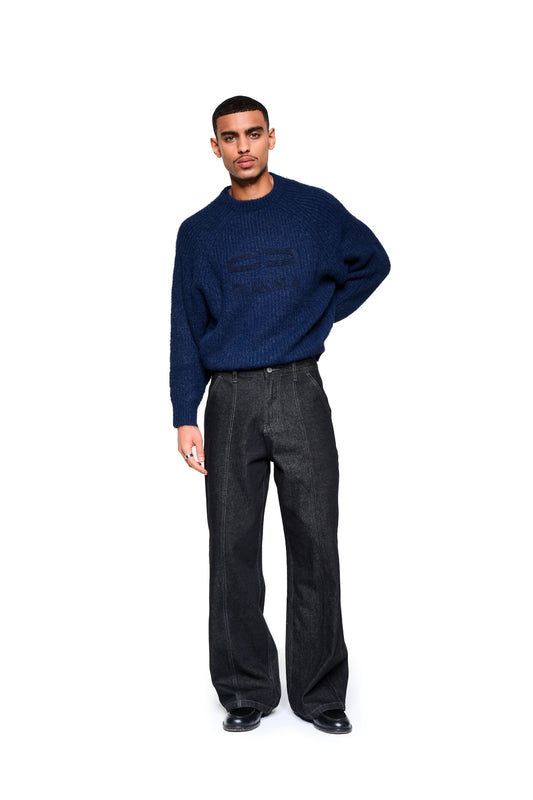 Männermodell trägt den Fuzzy Knit Sweater Navy Blue mit großer Logo-Stickerei, kombiniert mit schwarzen Jeans und Lederschuhen.