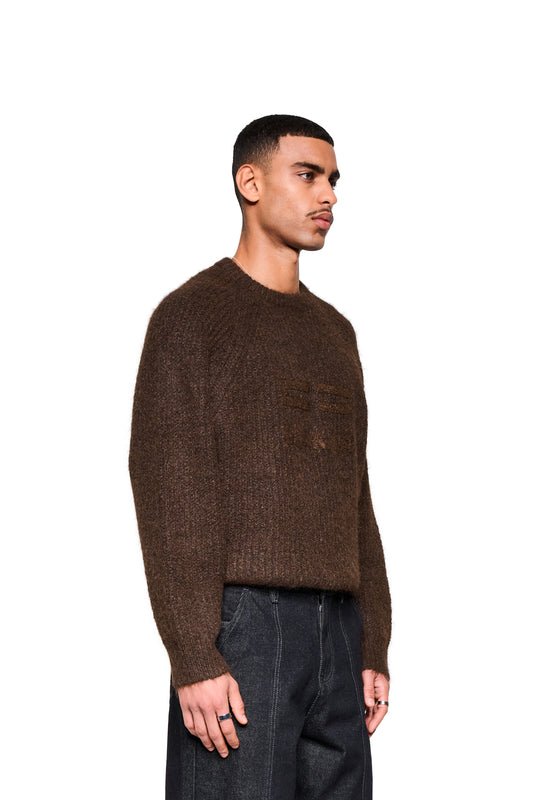 Junger Mann im Fuzzy Knit Sweater Brown mit cropped, boxy Silhouette und großer Logo-Stickerei, kombiniert mit dunklen Jeans.