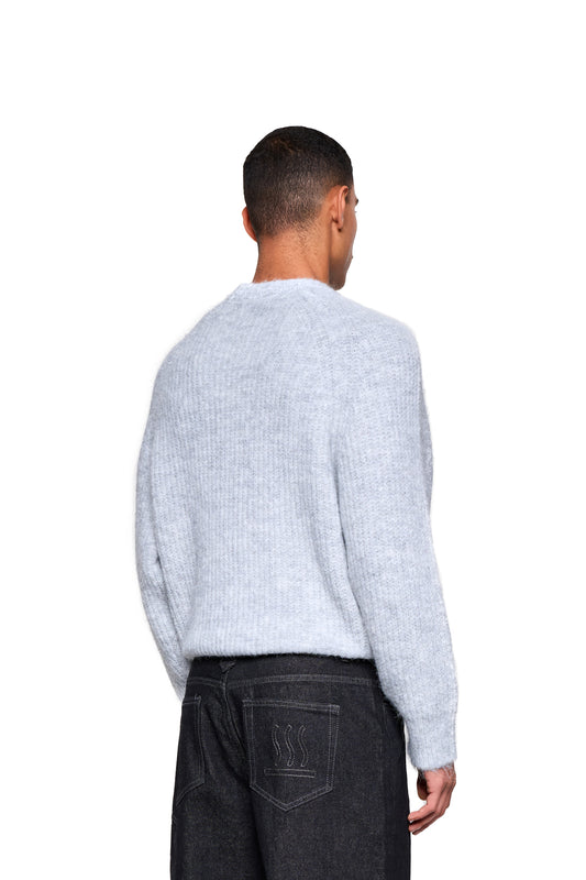 Rückansicht eines Manns im Fuzzy Knit Sweater Gray mit gerippter Textur, kombiniert mit Jeans mit Wellenstickerei auf der Tasche.