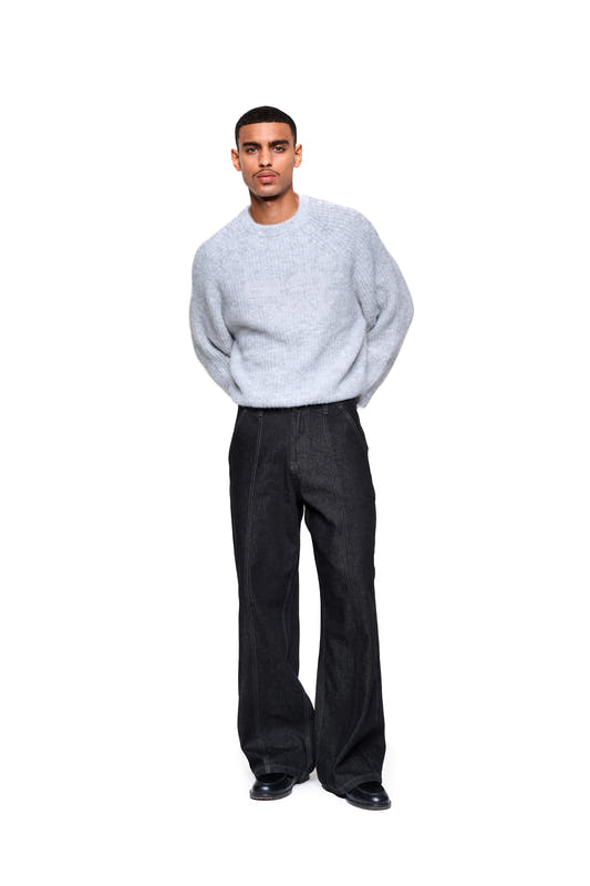 Man wearing a gray fuzzy knit sweater—cropped and boxy, with large embroidered logo on the front—paired with dark, wide-leg pants and black leather shoes.