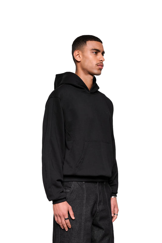 Ein junger Mann trägt den Mokka Hoodie mit Kängurutasche und silbernem Schmuck, der Komfort und weniger Reibung durch spezielle Nahtkonstruktion bietet.