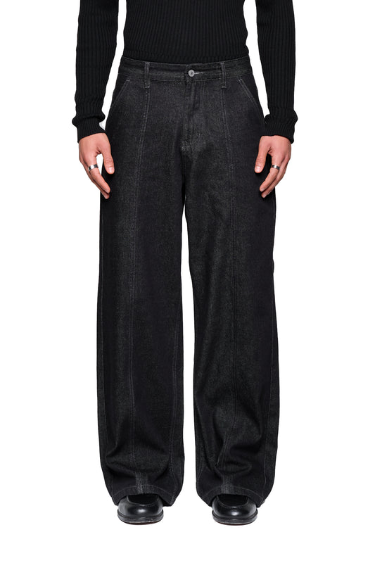 Modell trägt Raw Denim Pants Black in lockerem Schnitt, mit französischen Taschen und markanten Nähten, kombiniert mit schwarzen Lederschuhen, zeigt stilvolle, urbane Ästhetik.